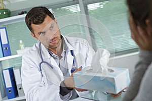 Doctor passing box tissues to patient