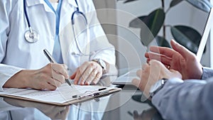 Doctor and patient discussing health concerns in medical office. Physician making notes on a clipboard. Medicine and