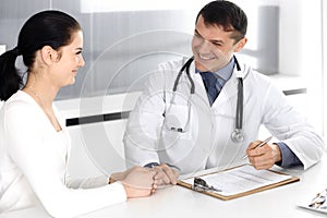 Doctor and patient discussing medical exam resoults at hospital office. Physician using clipboard for filling up