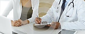 Doctor and patient discussing medical exam results while sitting at the desk in clinic, close-up. Male physician using