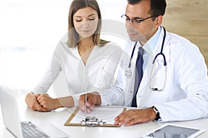 Doctor and patient discussing the results of a physical examination while sitting at a desk in a clinic. A male doctor