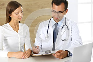 Doctor and patient discussing the results of a physical examination while sitting at a desk in a clinic. A male doctor