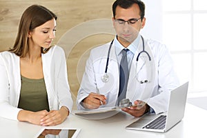 Doctor and patient discussing the results of a physical examination while sitting at a desk in a clinic. A male doctor