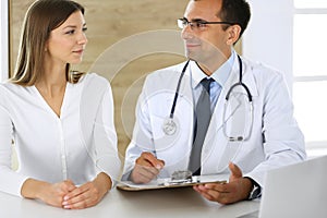 Doctor and patient discussing the results of a physical examination while sitting at a desk in a clinic. A male doctor