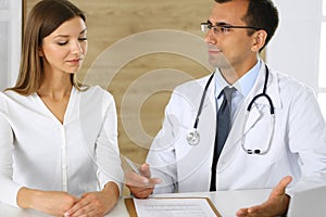 Doctor and patient discussing the results of a physical examination while sitting at a desk in a clinic. A male doctor