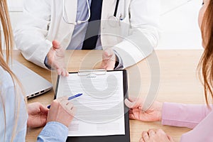 Doctor and patient are discussing something, hands at the table. Medical insurance. Doc sitting in cabinet. Man in white uniform.