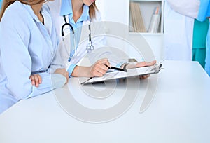 Doctor and patient discussing something, just hands at the table, white background. Physician pointing into clipboard