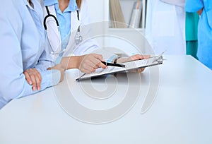 Doctor and patient discussing something, just hands at the table, white background. Physician pointing into clipboard