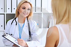 Doctor and patient discussing something while phisician pointing into medical history form at clipboard