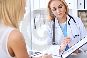 Doctor and patient discussing something while phisician pointing into medical history form at clipboard