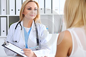 Doctor and patient discussing something while physician pointing into medical history form at clipboard