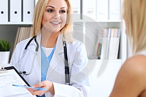 Doctor and patient discussing something while physician pointing into medical history form at clipboard