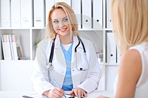 Doctor and patient discussing something while sitting at the table at hospital. Medicine and health care concept