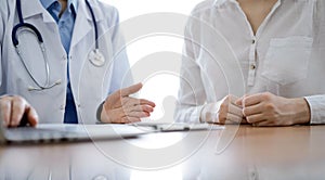 Doctor and patient discussing something while using laptop computer and sitting near each other at the wooden desk in