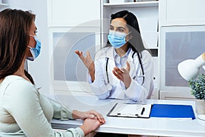 Doctor and patient in face masks discussing health problems while sitting at the table in medical center