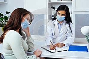 Doctor and patient in face masks discussing health problems while sitting at the table in medical center