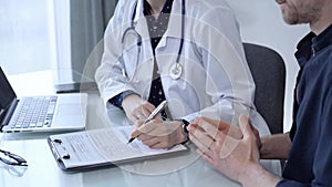 Doctor and patient. Female physician is sitting at the glass table, listening a senior man and writing medication