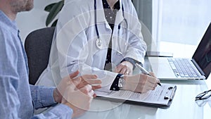 Doctor and patient. Female physician is sitting at the glass table, listening a senior man and writing medication