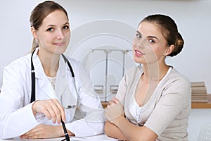 Doctor and patient having a pleasure talk while sitting at the desk at hospital office. Healthcare and medicine concept