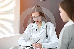 Doctor and patient in hospital. Physician filling up medication history records while talking with young woman