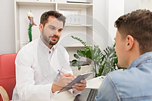 Doctor and patient in medical office. Therapist talking to patient in office, taking notes, writing prescription