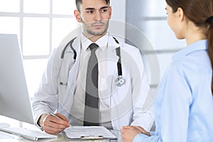 Doctor and patient. Physician man filling up medication history records form while sitting at the glass desk in medical