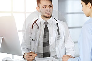 Doctor and patient. Physician man filling up medication history records form while sitting at the glass desk in medical