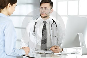 Doctor and patient. Physician man filling up medication history records form while sitting at the glass desk in medical