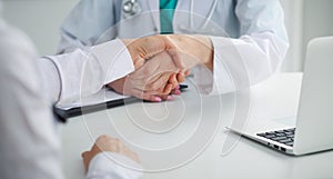 Doctor and patient shaking hands, close-up. Physician talking about medical examination results. Medicine, healthcar