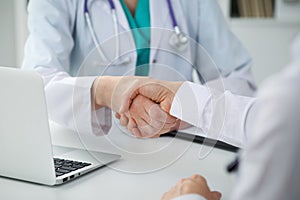 Doctor and patient shaking hands, close-up. Physician talking about medical examination results. Medicine, healthcar