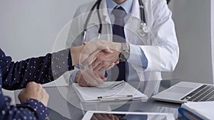 Doctor and patient are shaking hands while sitting at the grey glass table in clinic. Perfect medical service. Agreement