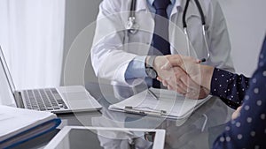 Doctor and patient are shaking hands while sitting at the grey glass table in clinic. Perfect medical service. Agreement