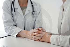 Doctor and patient sitting at the desk in clinic office. The focus is on female physician& x27;s hands reassuring woman