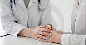 Doctor and patient sitting at the desk in clinic office. The focus is on female physician& x27;s hands reassuring woman