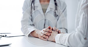 Doctor and patient sitting at the desk in clinic office. The focus is on female physician& x27;s hands reassuring woman