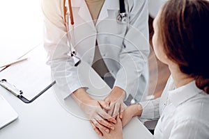 Doctor and patient sitting at the desk in clinic office. The focus is on female physician& x27;s hands reassuring woman