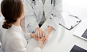 Doctor and patient sitting at the desk in clinic office. The focus is on female physician& x27;s hands reassuring woman