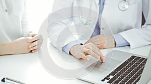 Doctor and patient sitting near each other at the desk in clinic. The focus is on female physician& x27;s hands using