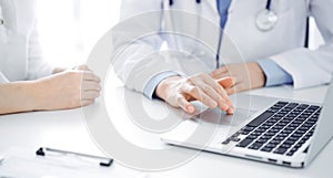 Doctor and patient sitting near each other at the desk in clinic. The focus is on female physician& x27;s hands using