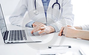 Doctor and patient sitting near each other at the desk in clinic. The focus is on female physician& x27;s hands using