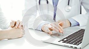 Doctor and patient sitting near each other at the desk in clinic. The focus is on female physician& x27;s hands using