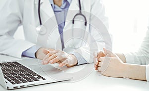 Doctor and patient sitting near each other at the desk in clinic. The focus is on female physician& x27;s hands using