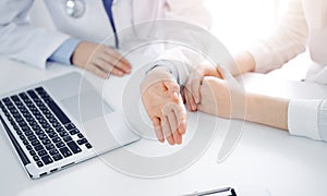 Doctor and patient sitting near each other at the desk in clinic. The focus is on female physician& x27;s hands using