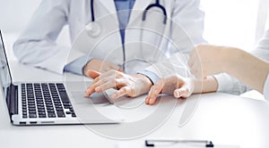 Doctor and patient sitting near each other at the desk in clinic. The focus is on female physician& x27;s hands using