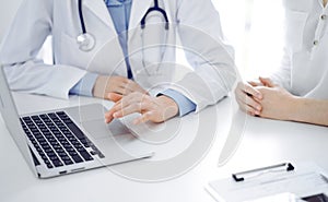 Doctor and patient sitting near each other at the desk in clinic. The focus is on female physician& x27;s hands using