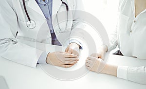 Doctor and patient sitting near each other at the desk in clinic. The focus is on female physician& x27;s hands using