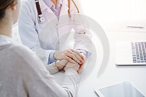 Doctor and patient sitting at the table in clinic office. The focus is on female physician& x27;s hands reassuring woman