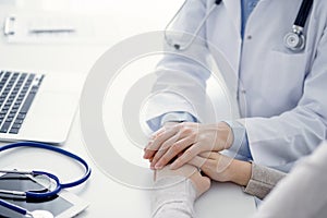 Doctor and patient sitting at the table in clinic office. The focus is on female physician& x27;s hands reassuring woman