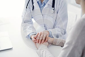 Doctor and patient sitting at the table in clinic office. The focus is on female physician& x27;s hands reassuring woman