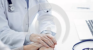 Doctor and patient sitting at the table in clinic office. The focus is on female physician& x27;s hands reassuring woman